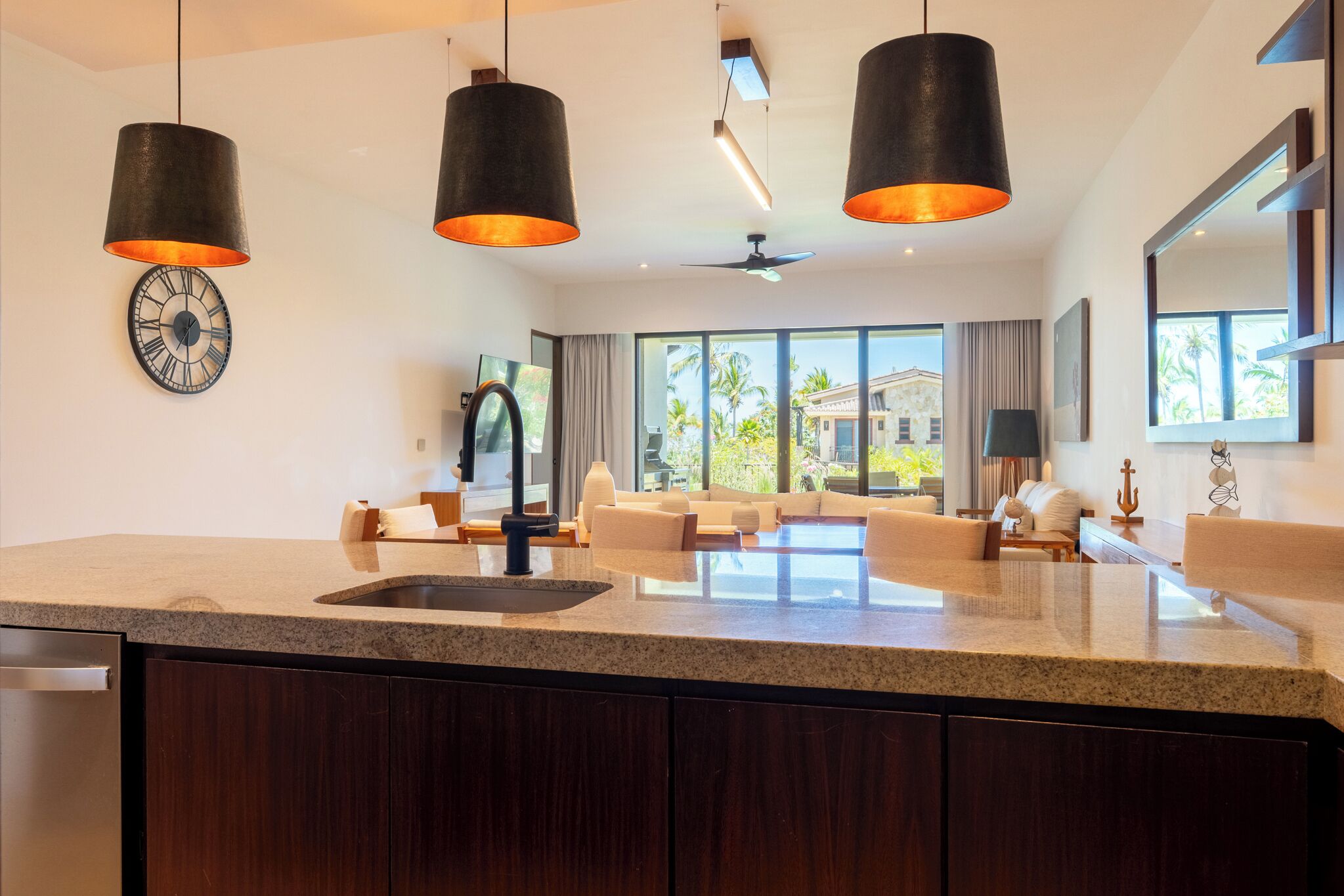 A modern kitchen with granite countertops, dark wooden cabinets, and pendant lighting.