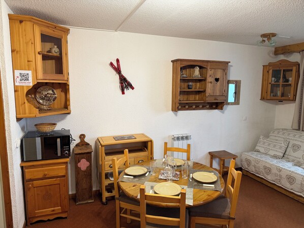 Un comedor con una mesa de madera dispuesta para cuatro personas, sillas alrededor y un aparador de madera con estantes superiores.