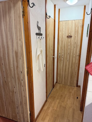 A hallway with wooden doors, a coat hanging on a hook, and a small table with a red checkered cloth.