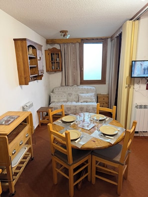 A cozy dining area with a wooden table set for four, a sofa, and a television mounted on the wall.