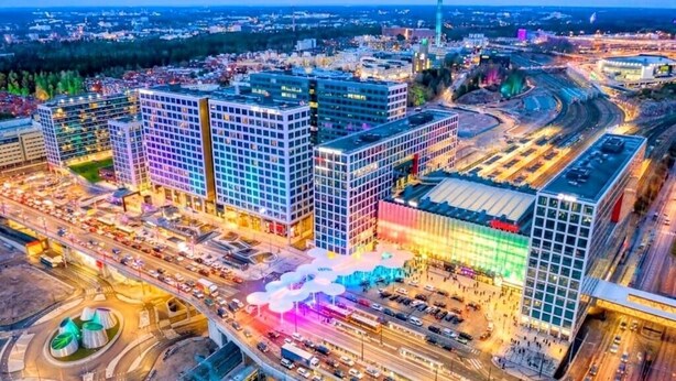 Stadsbeeld met moderne gebouwen, een rotonde en een groot parkeergebied.