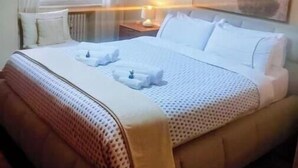 Een hotelkamer met een bed, nachtkastje, lamp, raam met gordijnen en een schilderij aan de muur.