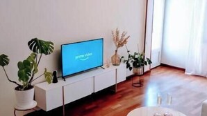 Een moderne woonkamer met een flatscreen televisie, houten vloer, een ronde salontafel en potplanten.