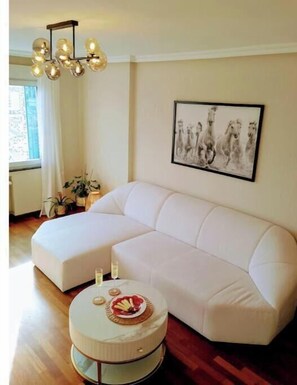 A modern living room with a white sectional sofa, a round coffee table with a plate of food, a chandelier, and a framed picture on the wall. - A step away from Gascona with Netflix and wifi VUT7221AS (Oviedo)