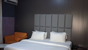 Una habitación de hotel con una cama, una butaca naranja, una mesita y un equipo de aire acondicionado.
