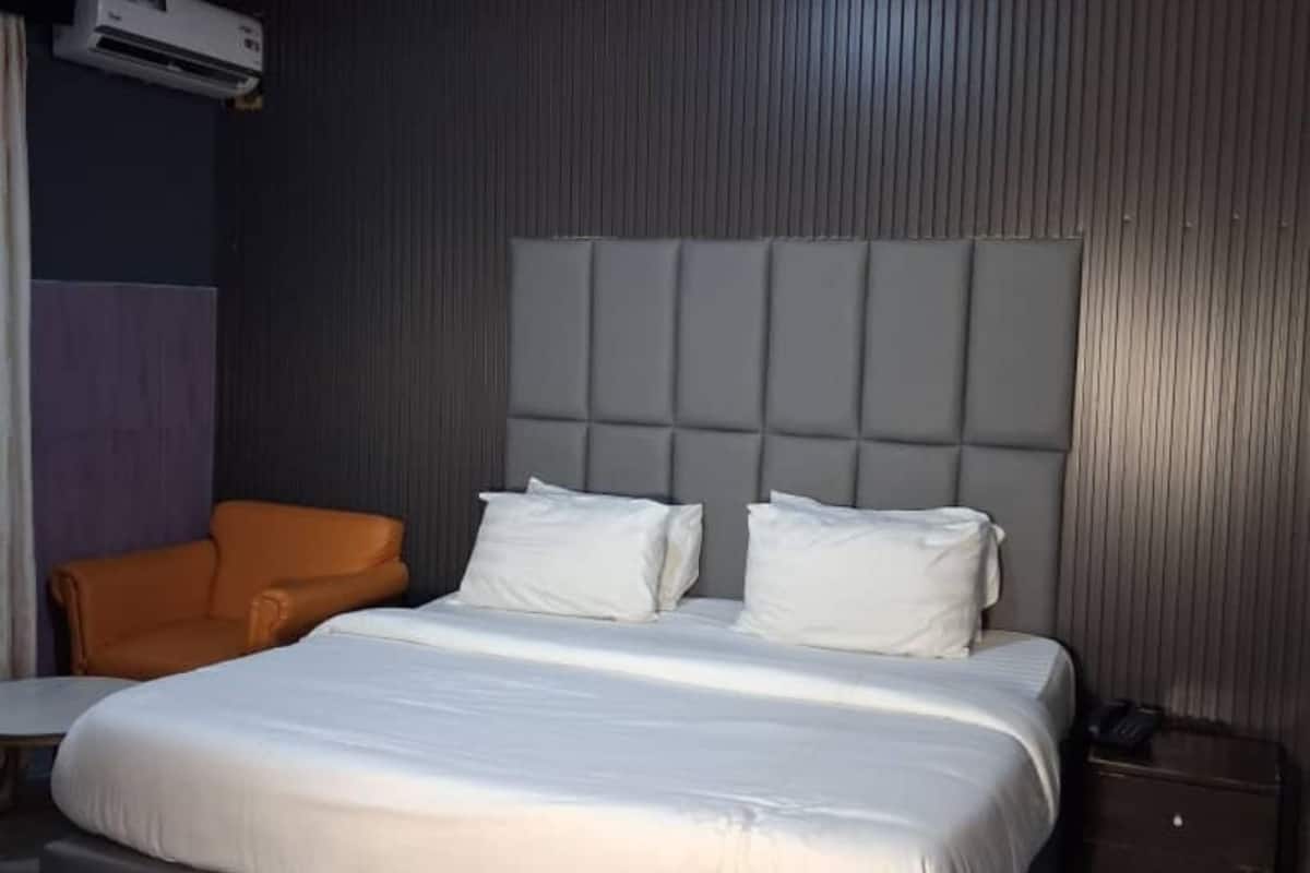 A hotel room with a bed, an orange chair, a small table, and an air conditioning unit.