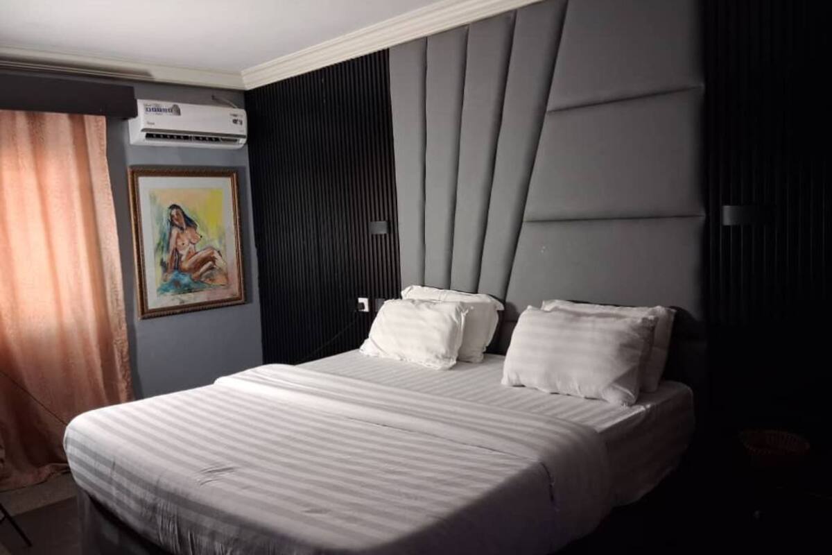 A hotel room with a large bed, a painting on the wall, and a modern headboard.