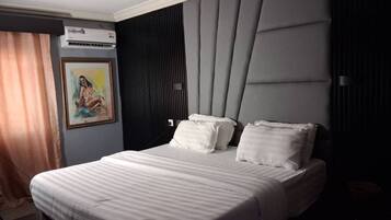 A hotel room with a large bed, a painting on the wall, and a modern headboard.