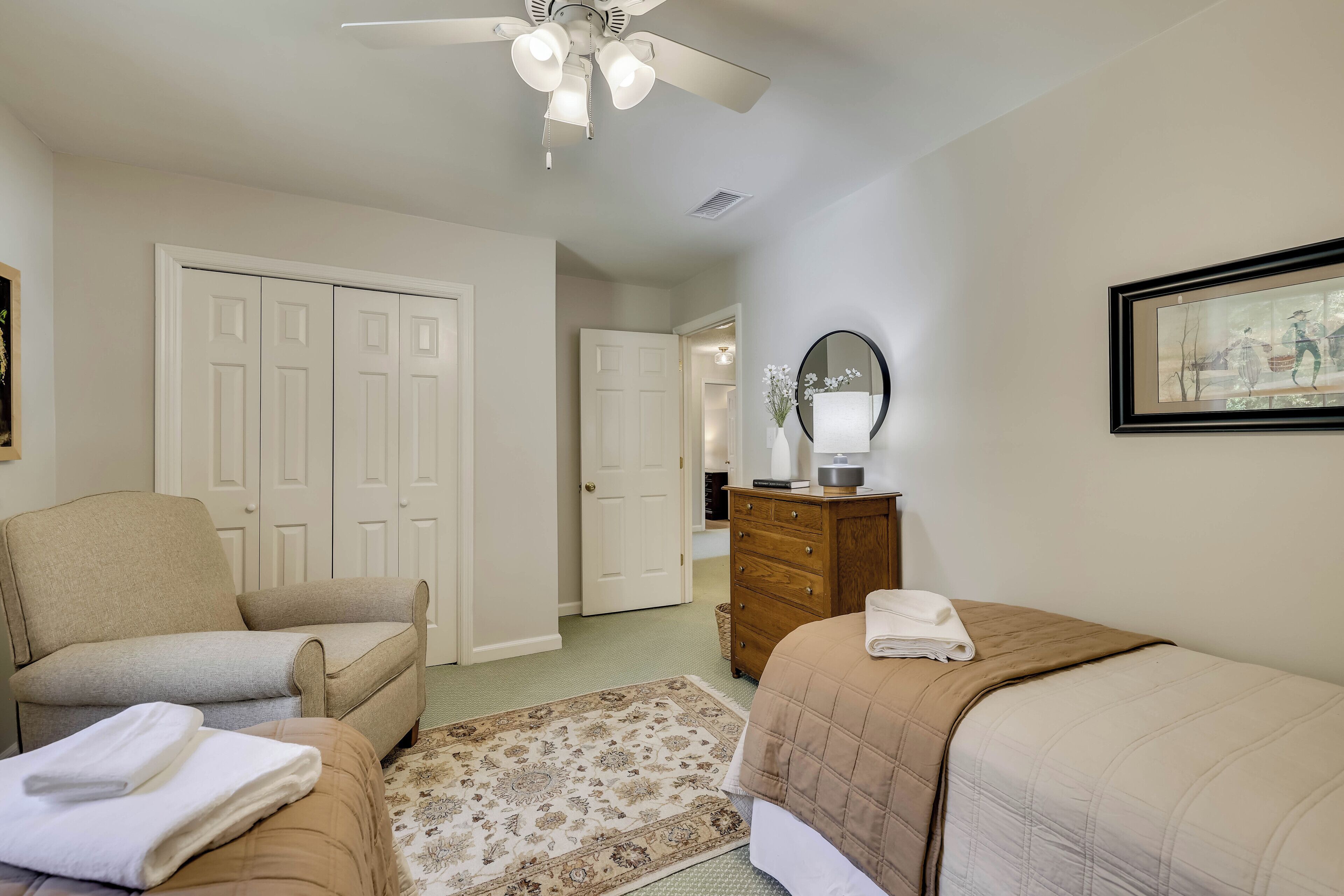 Une chambre à coucher comprenant un lit, une chaise, une commode, un ventilateur de plafond et une porte donnant sur une autre pièce.