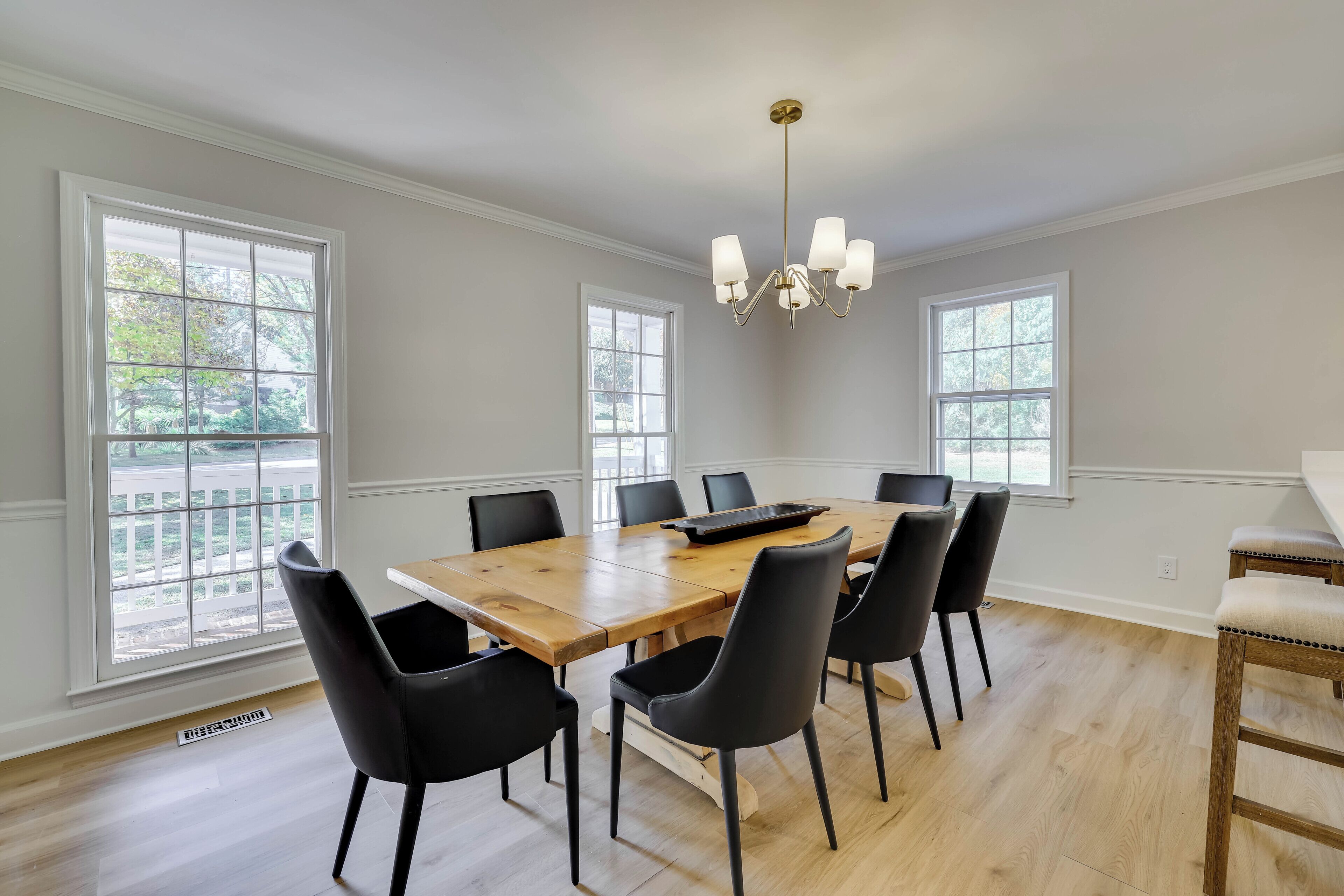 A dining room with a wooden table, black chairs, a chandelier, and large windows.