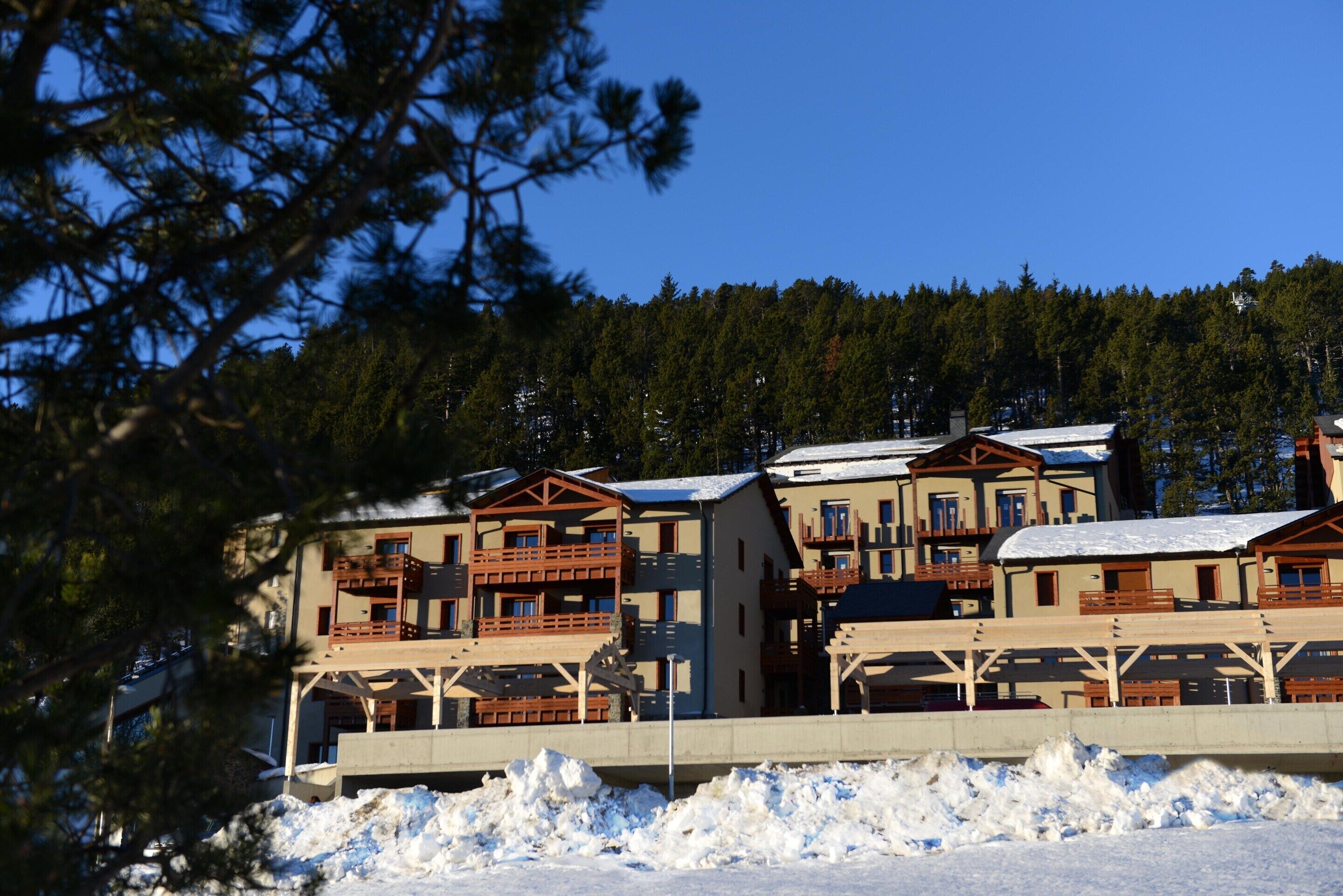 Eine mehrstöckige Lodge mit Balkonen, eingebettet in eine verschneite Winterlandschaft mit Wald im Hintergrund.