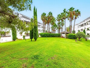 Un patio cuidado con césped, altas palmeras y un edificio blanco con balcones.