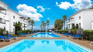 A swimming pool with lounge chairs and umbrellas, surrounded by white buildings and palm trees. - San-nicolao Beachfront Stay for 4 (San-Nicolao)