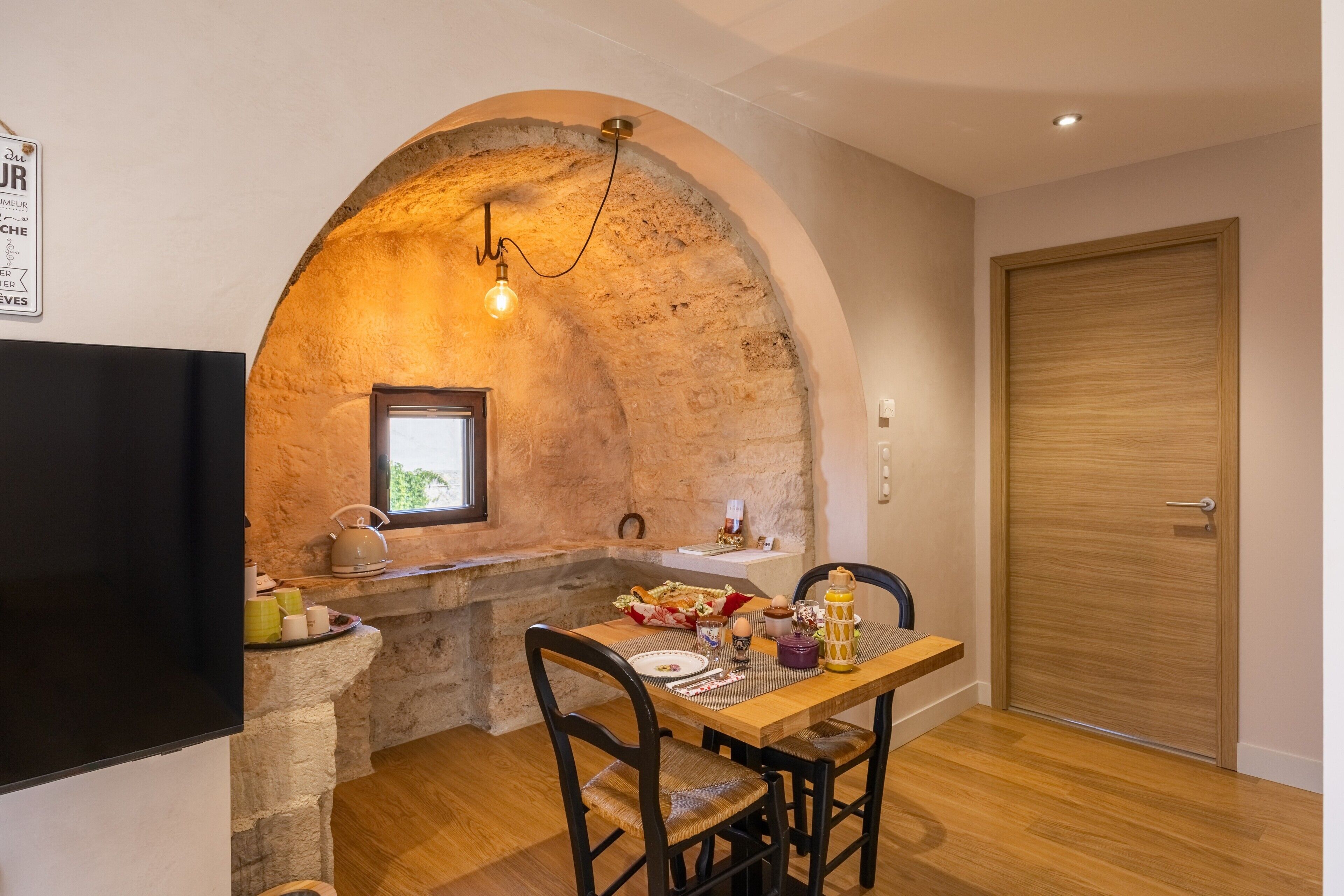 Un comedor con un arco de piedra, una mesa de madera, sillas y un televisor en la pared.