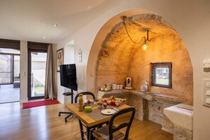 Zona pranzo con arco in pietra, tavolo in legno, sedie, televisore e finestra con vista.