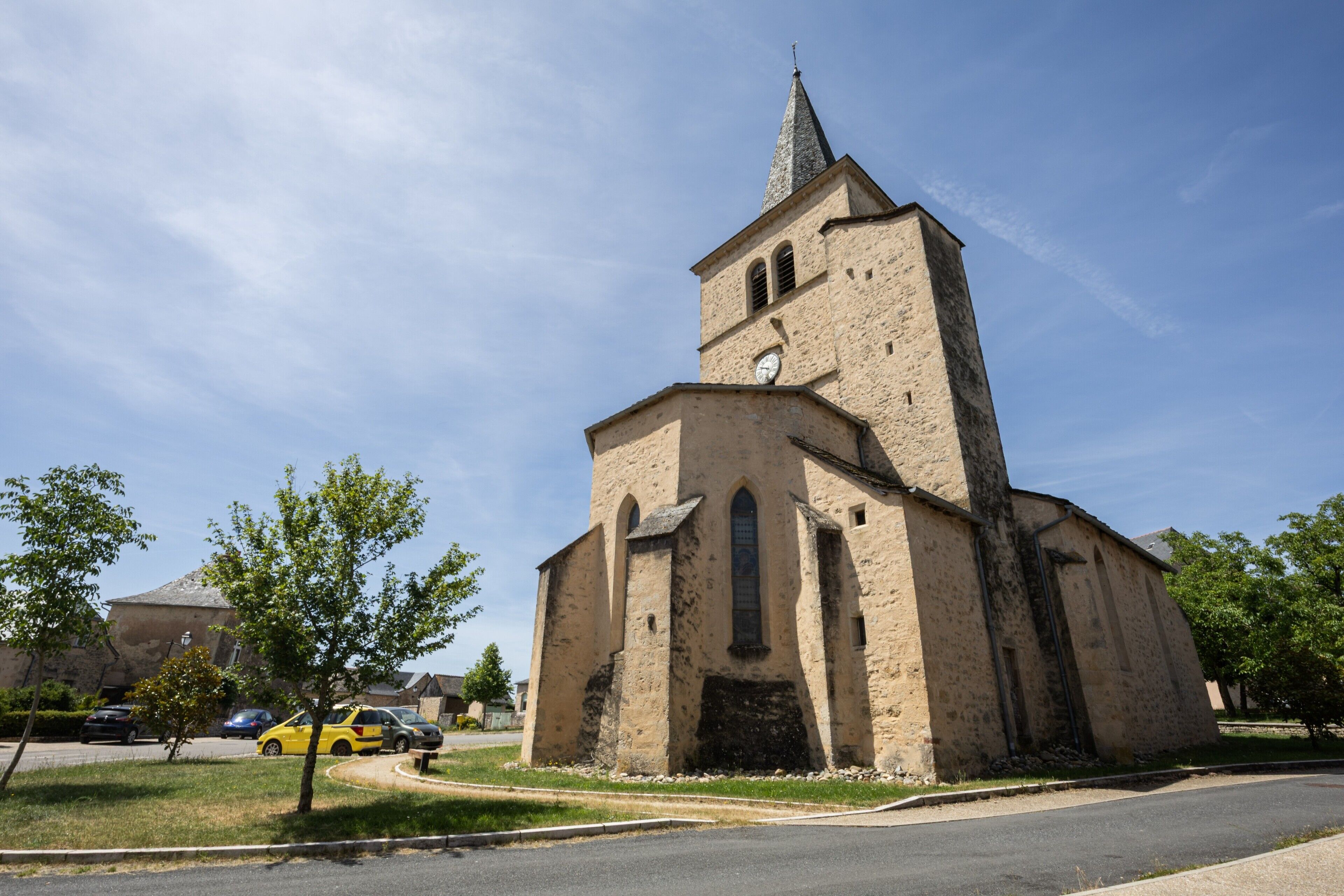 Eine Kirche mit einem markanten Turm, einem klaren Himmel und einer Straße mit parkenden Autos.