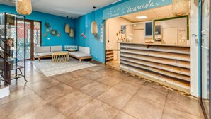 A reception area with a blue wall, a reception desk, a sofa, and hanging wicker lamps. - Chic Coastal Pool View Apartment for 6 (Le Grau-Du-Roi)
