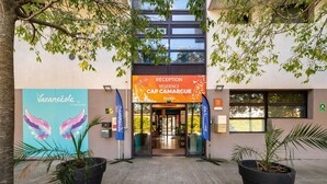 A hotel entrance with a reception desk, a sign for 'RECEPTION RÉSIDENCE CAP CAMARGUE,' and two potted plants on either side. - Chic Coastal Pool View Apartment for 6 (Le Grau-Du-Roi)