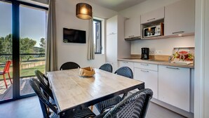 Et moderne køkken med spisebord og stole, et tv ophængt på væggen og udsigt til det fri.