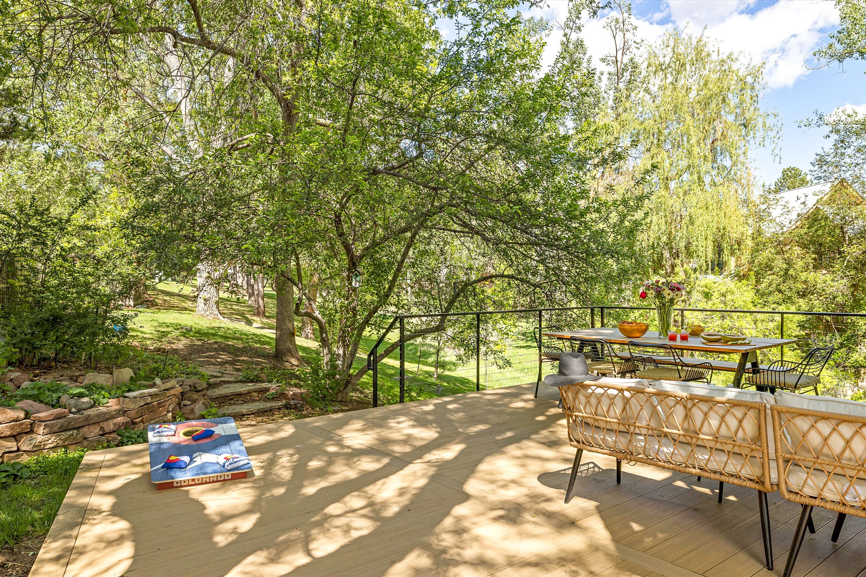 An outdoor patio with wicker furniture, a table with a vase, and a view of a park.