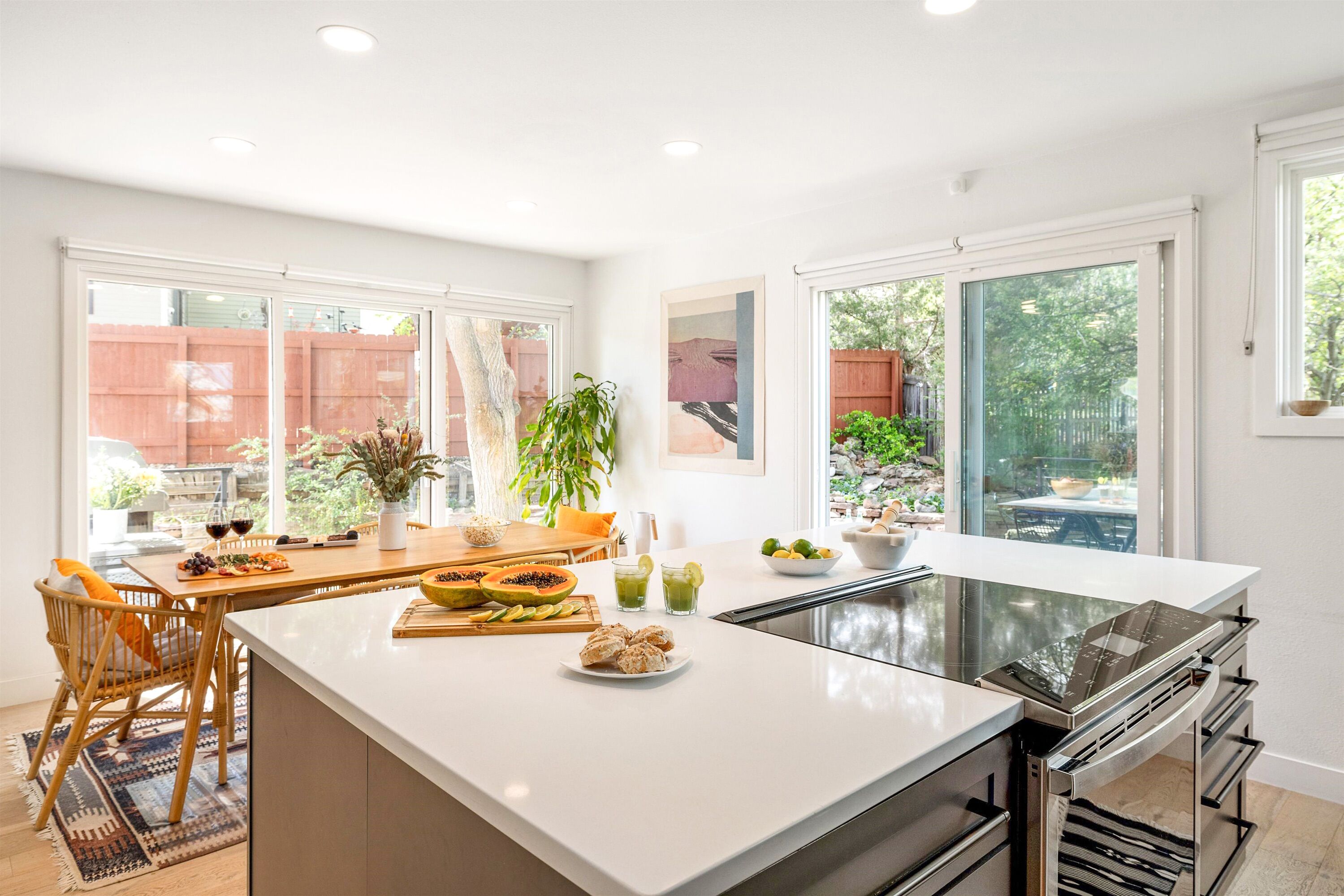 Una cocina moderna con una isla grande, armarios blancos y amplios ventanales que ofrecen vistas al exterior.