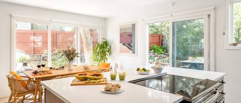 Una cocina moderna con una isla grande, armarios blancos y amplios ventanales que ofrecen vistas al exterior.