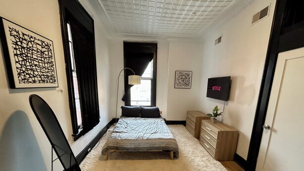 Un dormitorio con cama, escritorio, silla, televisor y obras de arte en las paredes.