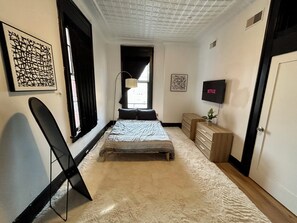 A bedroom with a bed, a desk, a chair, a TV, and artwork on the walls. - Modern Downtown Loft w/ Spiral Staircase O.T.R. (Cincinnati)