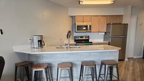 A modern kitchen with a central island, stainless steel appliances, and wooden stools. - Recently renovated lake View Condo with balcony (Port Clinton)