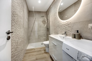 A modern bathroom with a walk-in shower, a toilet, and a sink with a mirror. - Apartment in the Center of Alvor (Alvor)