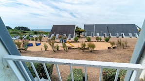 Vista costera con cabañas de playa, una zona arenosa con plantas y un estacionamiento.