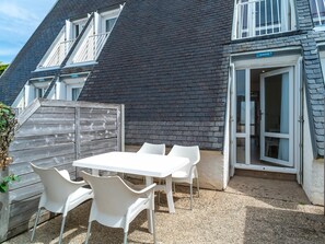 A patio with a table and chairs, a wooden fence, and a building with a dark roof and a door labeled 'A0010'. - Duplex, 200m to Falaise Beach (Guidel)