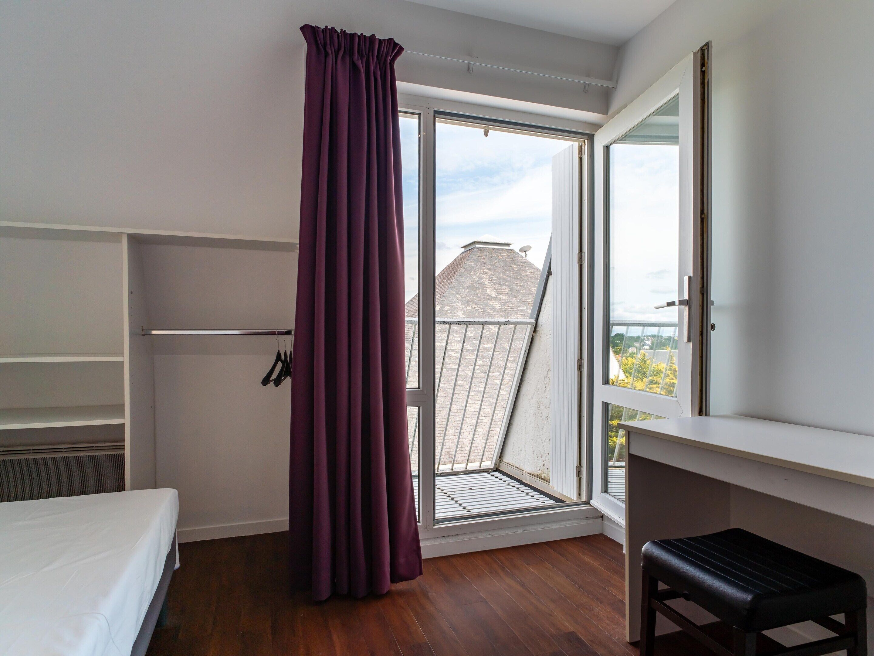 Una habitación con cama, escritorio, ventana con vistas y balcón.