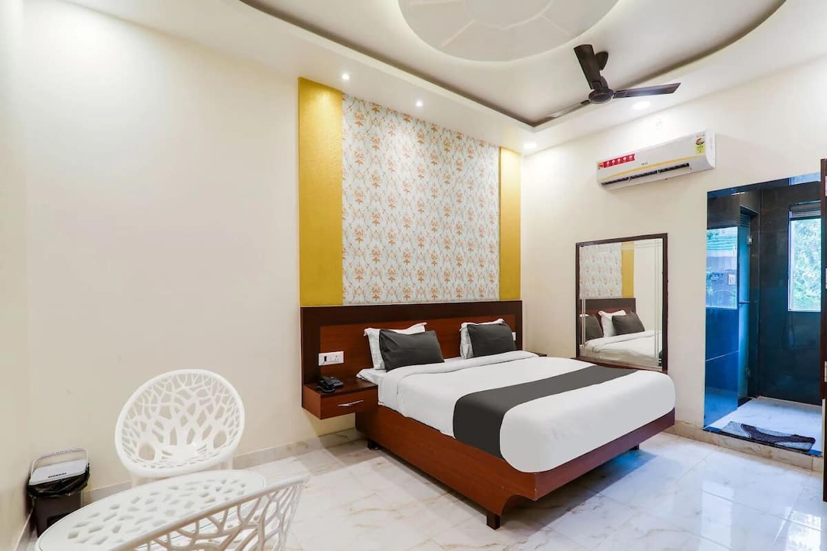 Habitación de hotel con cama, una mesita pequeña, dos sillas, ventilador de techo, equipo de aire acondicionado y un espejo grande.