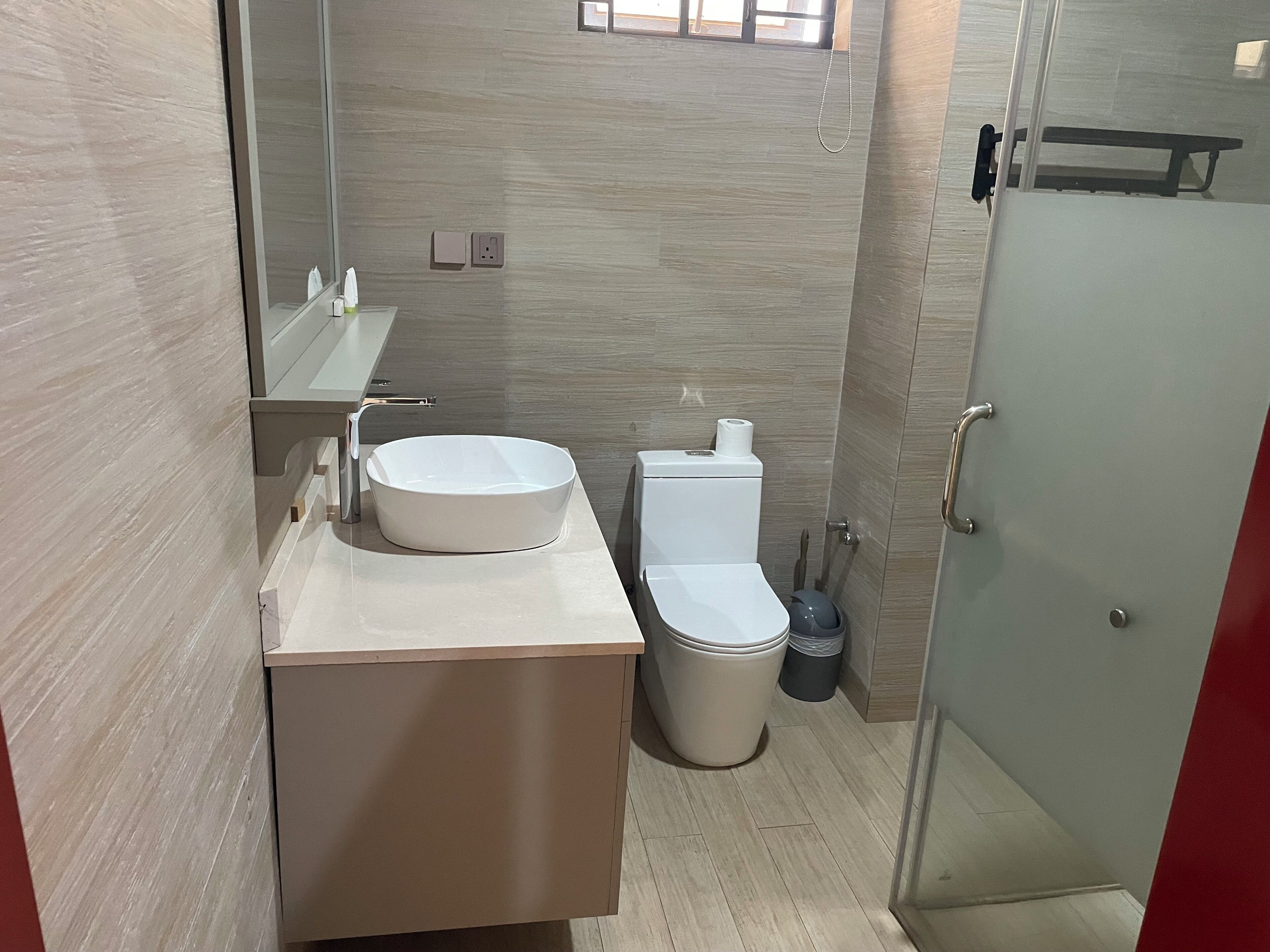 A modern bathroom with a round sink, toilet, and a glass shower enclosure.