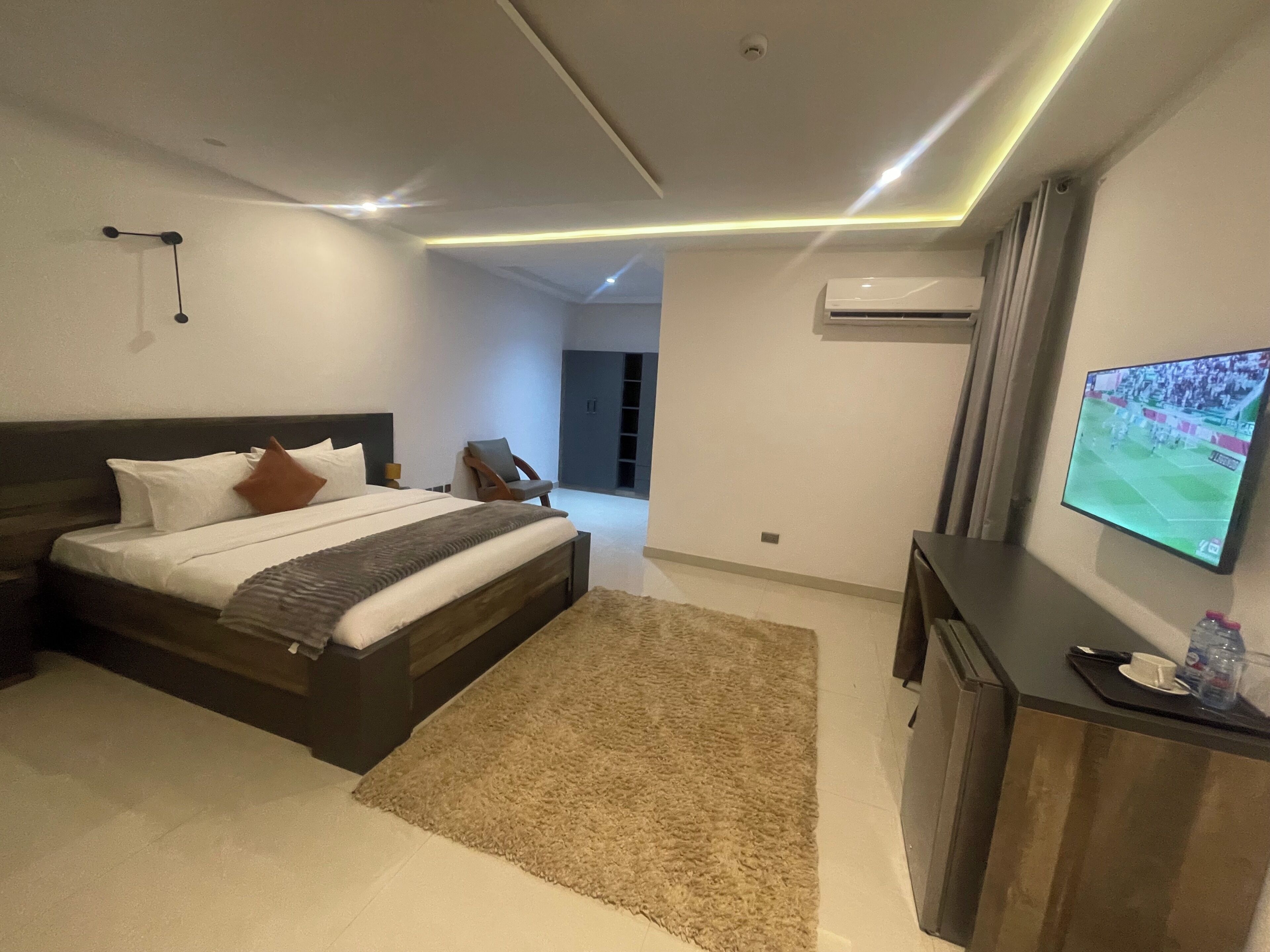A modern hotel room with a large bed, a flat-screen TV, a desk, and an air conditioning unit.