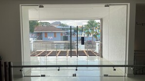 A modern hotel room with a large glass door leading to a balcony, a metal railing, and a view of the street and buildings outside.