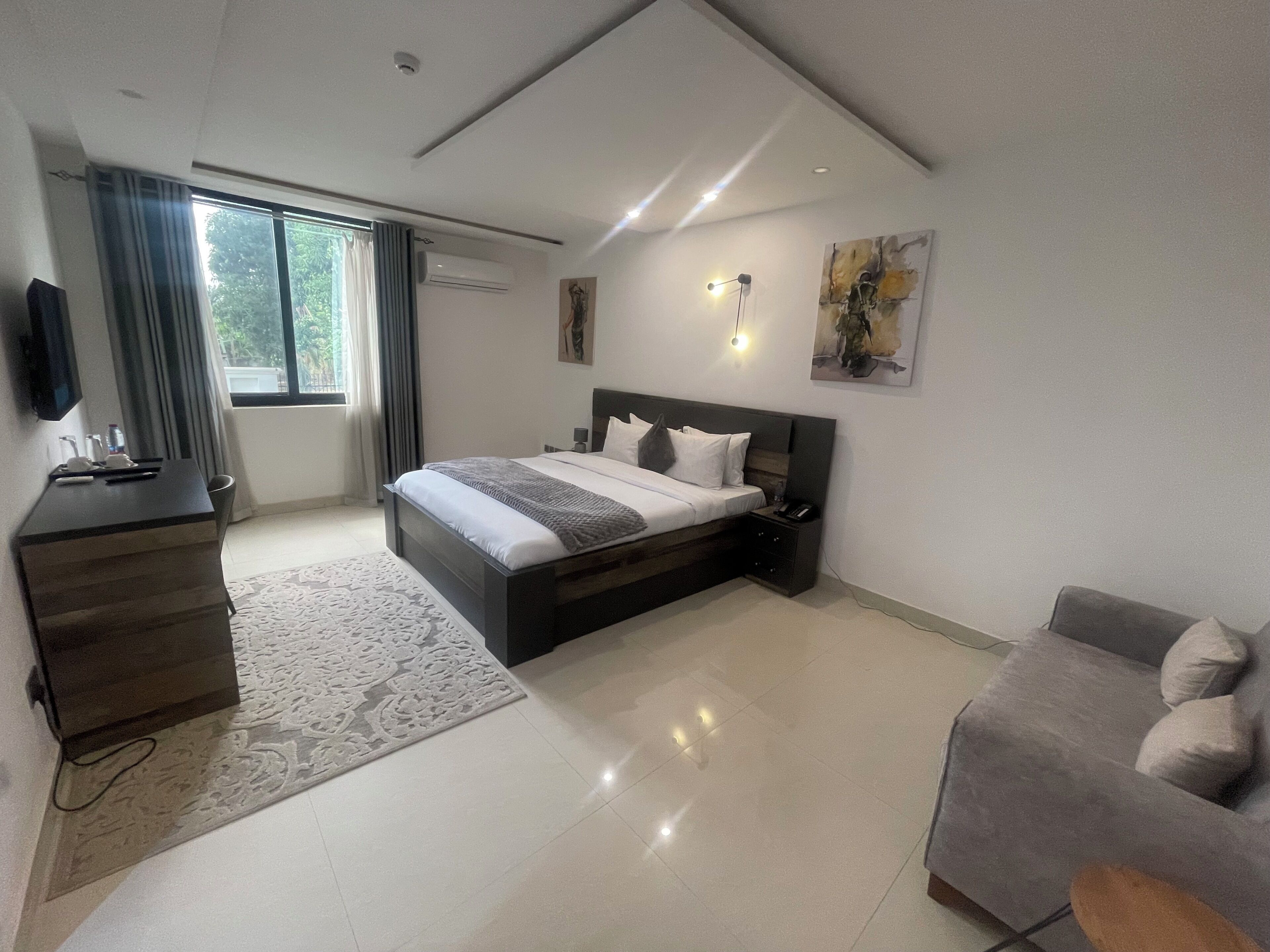 A modern hotel room with a large bed, a desk, a sofa, and a TV.