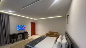 A modern hotel room with a bed, a TV, a desk, and a sofa.