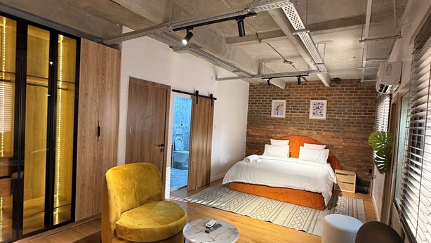 Een moderne slaapkamer met een bed, een gele fauteuil, een zwarte fauteuil en een klein tafeltje.