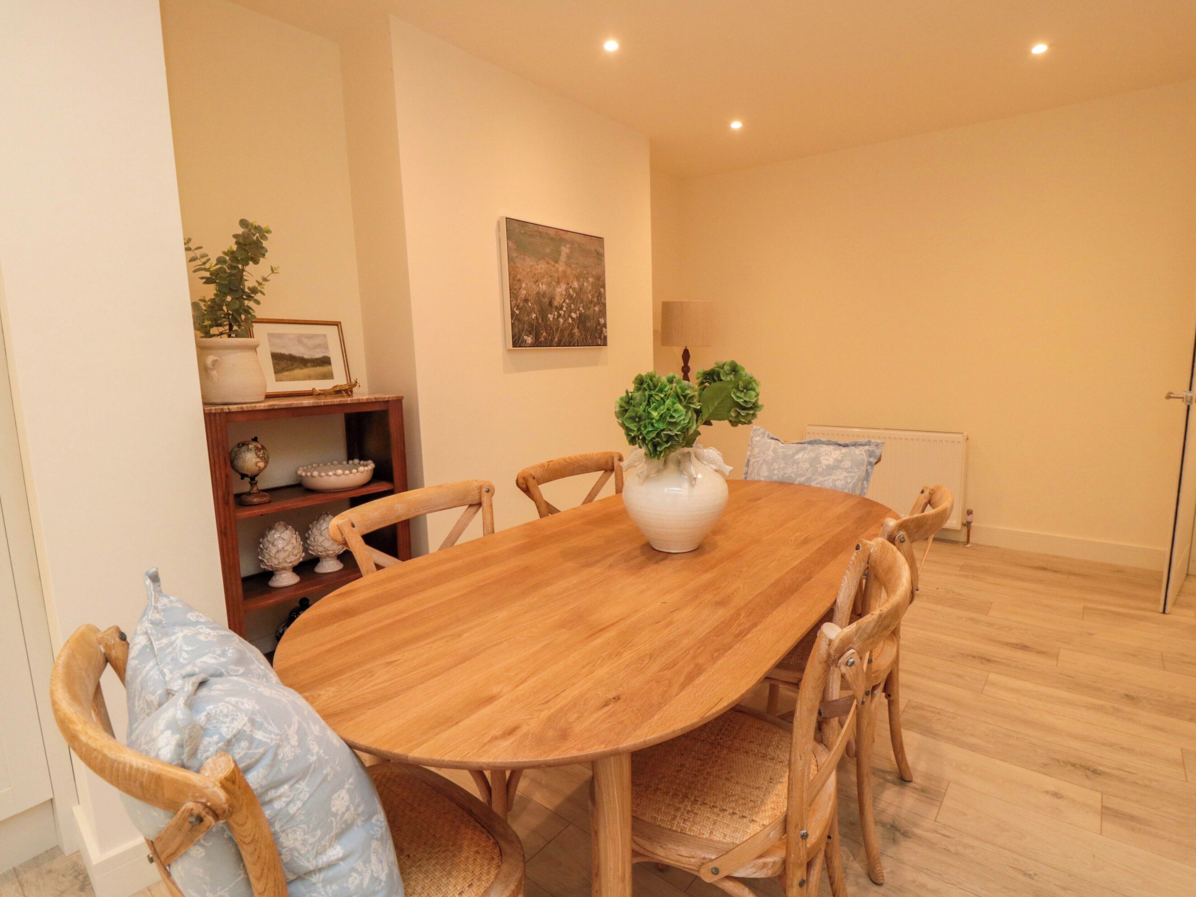 A dining area with a wooden table and chairs, a vase with green plants, a globe, and a framed picture on the wall.