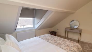 A bedroom with a bed, a window, a radiator, a dresser, and a mirror.