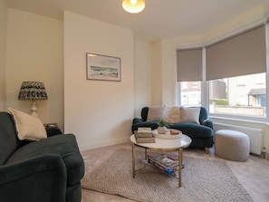 A living room with a sofa, a coffee table, a lamp, a framed picture, and a window with a view of buildings. - Trafalgar II (Scarborough)