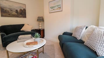 A living room with a dark green sofa, a white coffee table, and a painting on the wall.