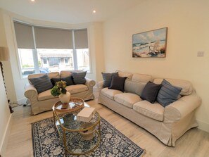 A living room with two beige sofas, a glass coffee table, a patterned rug, and a painting of a beach scene. - Trafalgar I (Scarborough)