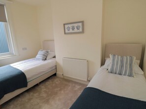A bedroom with two single beds, a radiator, a framed picture on the wall, and a window. - Trafalgar I (Scarborough)