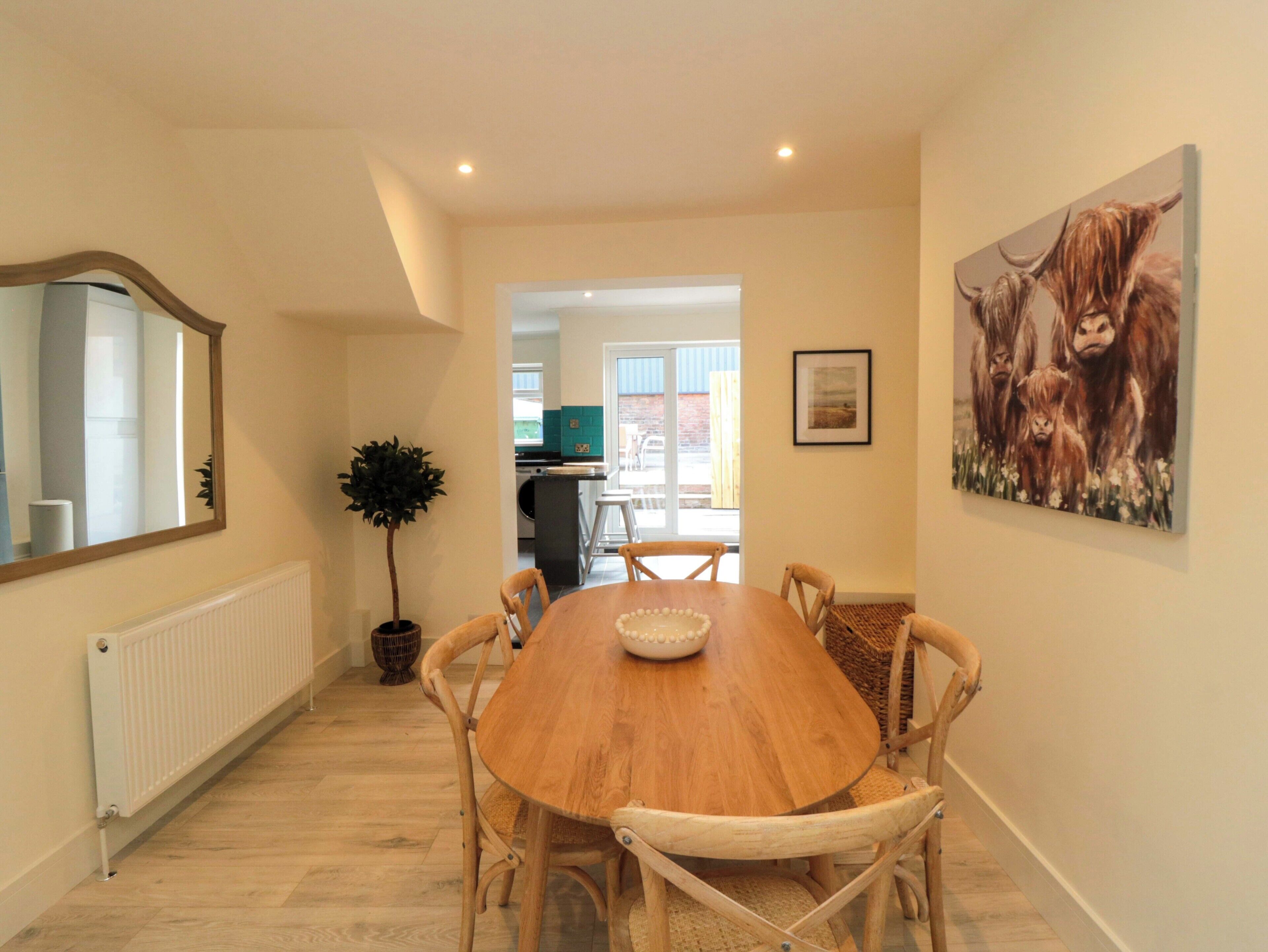 A dining area with a wooden table, chairs, a potted plant, and a painting on the wall.