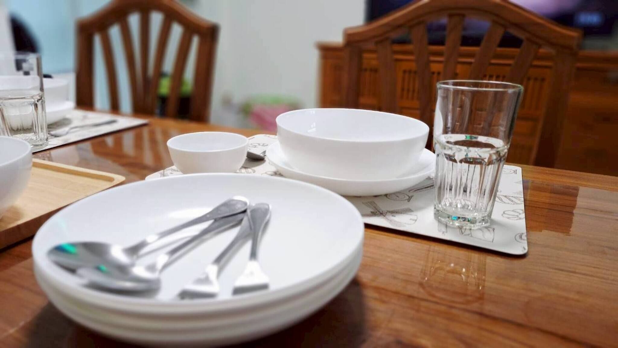 A dining table with white plates, cutlery, and a glass of water.