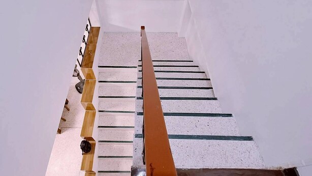 Un escalier avec une main courante en bois et une balustrade en métal, menant à un palier avec un mur blanc.