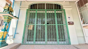 Une porte en métal verte, surmontée d’une arche décorative, une petite plaque fixée au mur sur la droite, et un escalier menant à la porte.